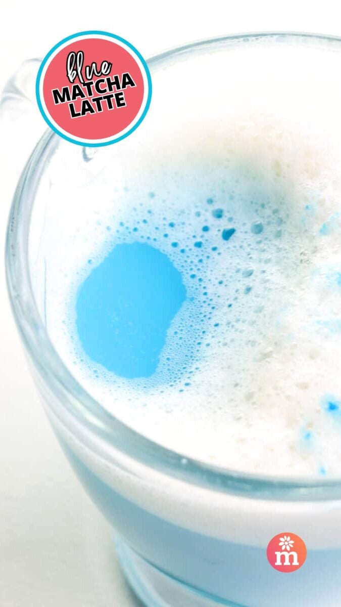 Looking down into a glass mug with blue tea and steamed soy milk on top. The text reads, Blue Matcha Latte.