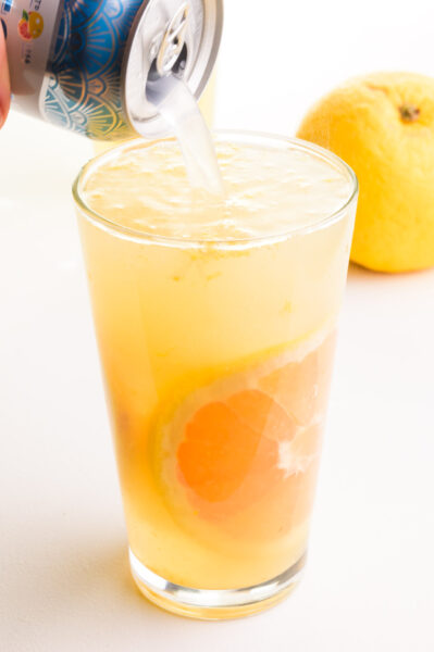 Bubbly sparkling water is being poured into a glass with a grapefruit green tea mixture.