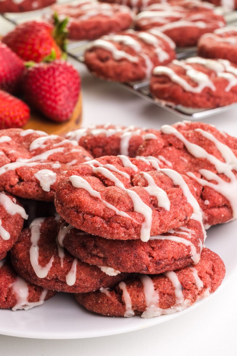 Vegan strawberry cookies sit on a pate. There are fresh strawberries and more cookies in the background.