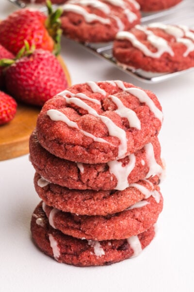 A stack of vegan strawberry cookies sit in front of fresh strawberries and more cookies in the background.