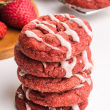 A stack of strawberry cookies sits in front of fresh strawberries.