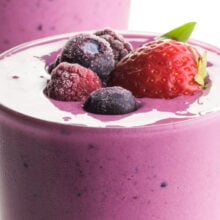 A closeup of a vibrant berry smoothie shows fresh and frozen fruit on top.