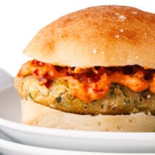 A closeup of a pesto veggie burger on a bun with lots of sun-dried tomato aioli on top.
