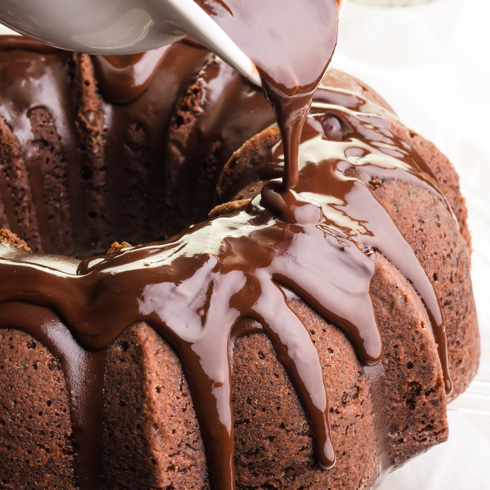 Chocolate sauce is being poured over a chocolate Bundt Cake.