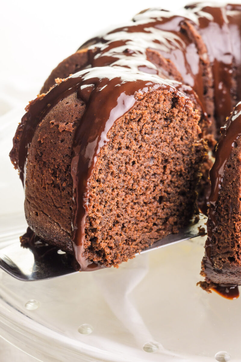 A slice of chocolate cake is being removed with a spatula from the pan holding the rest of the cake.