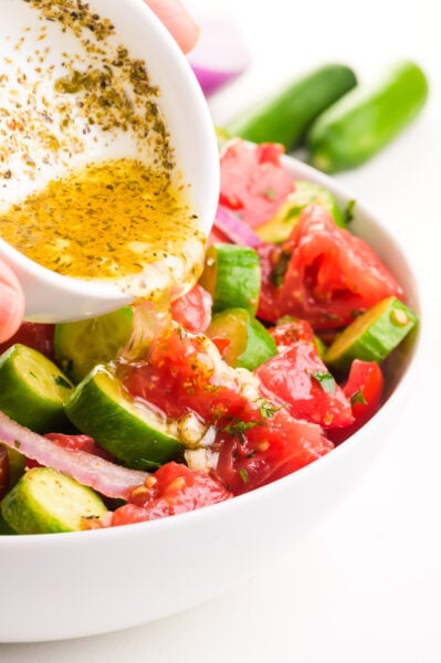 Dressing is being poured over a tomato cucumber salad.
