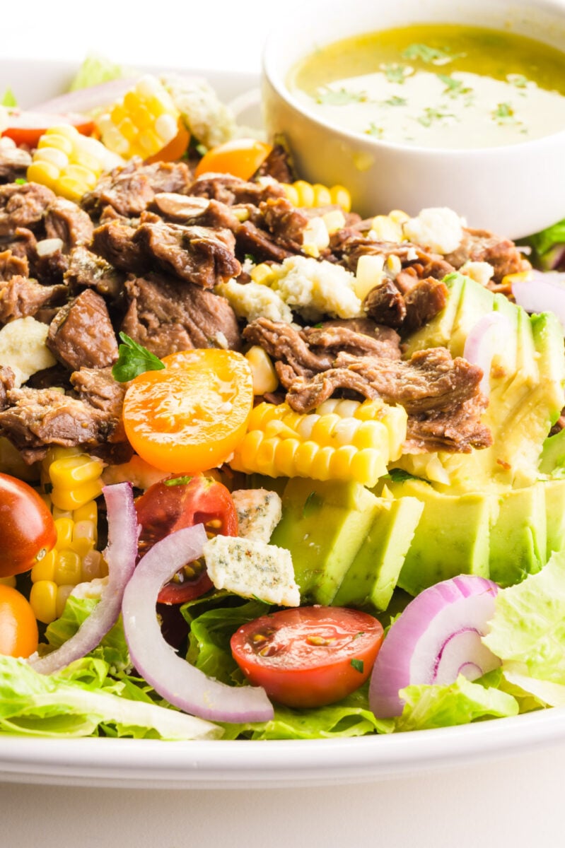 A closeup of a vegan steak salad features avocados, onions, and more.