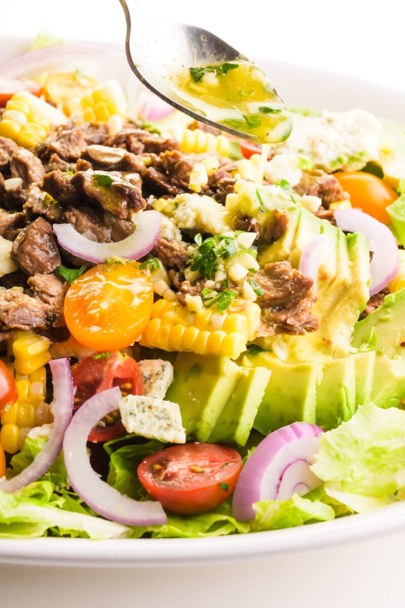 Dressing is being drizzled from a spoon over a salad.