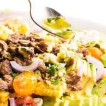 Dressing is being drizzled from a spoon onto a veggie steak salad.
