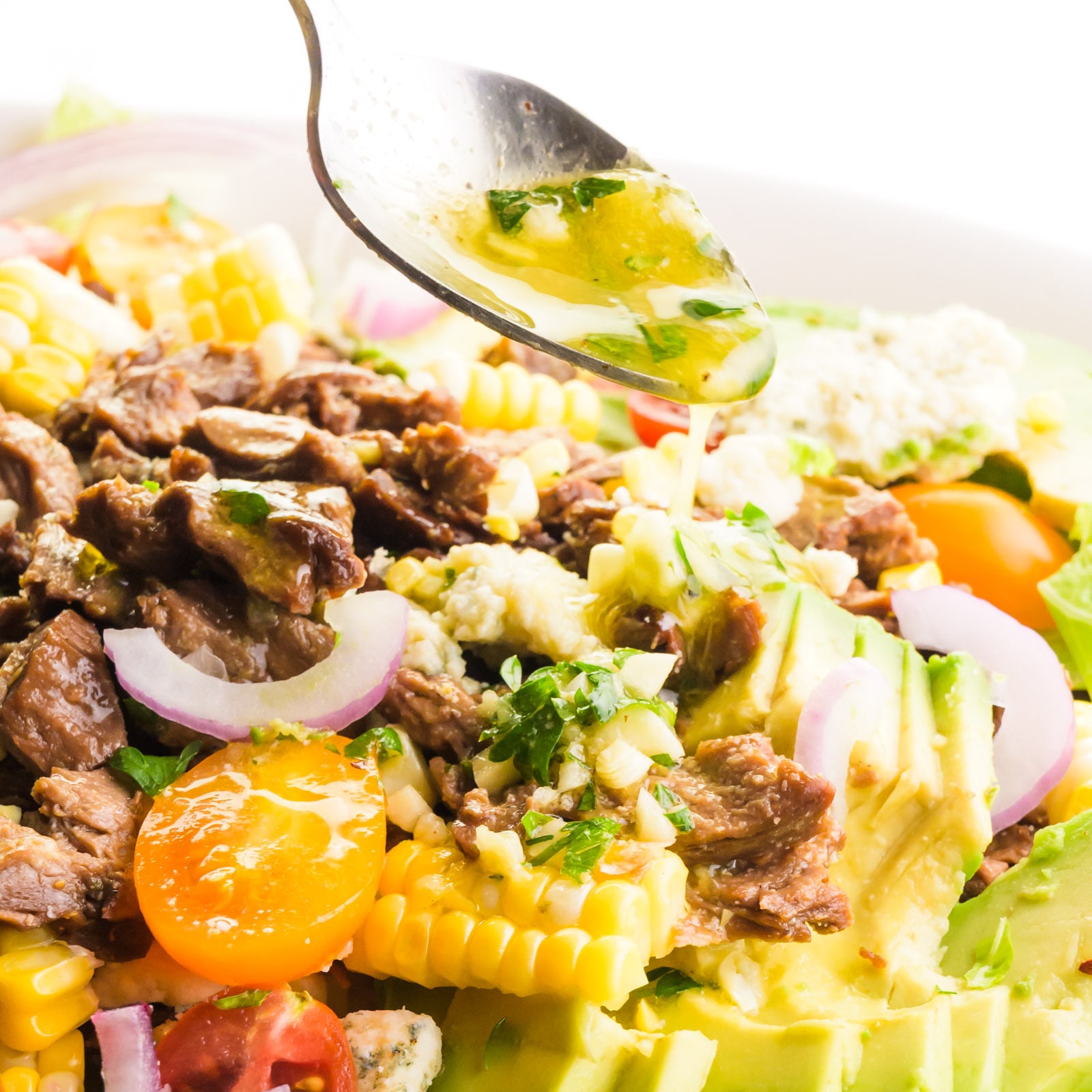 Dressing is being drizzled from a spoon onto a veggie steak salad.