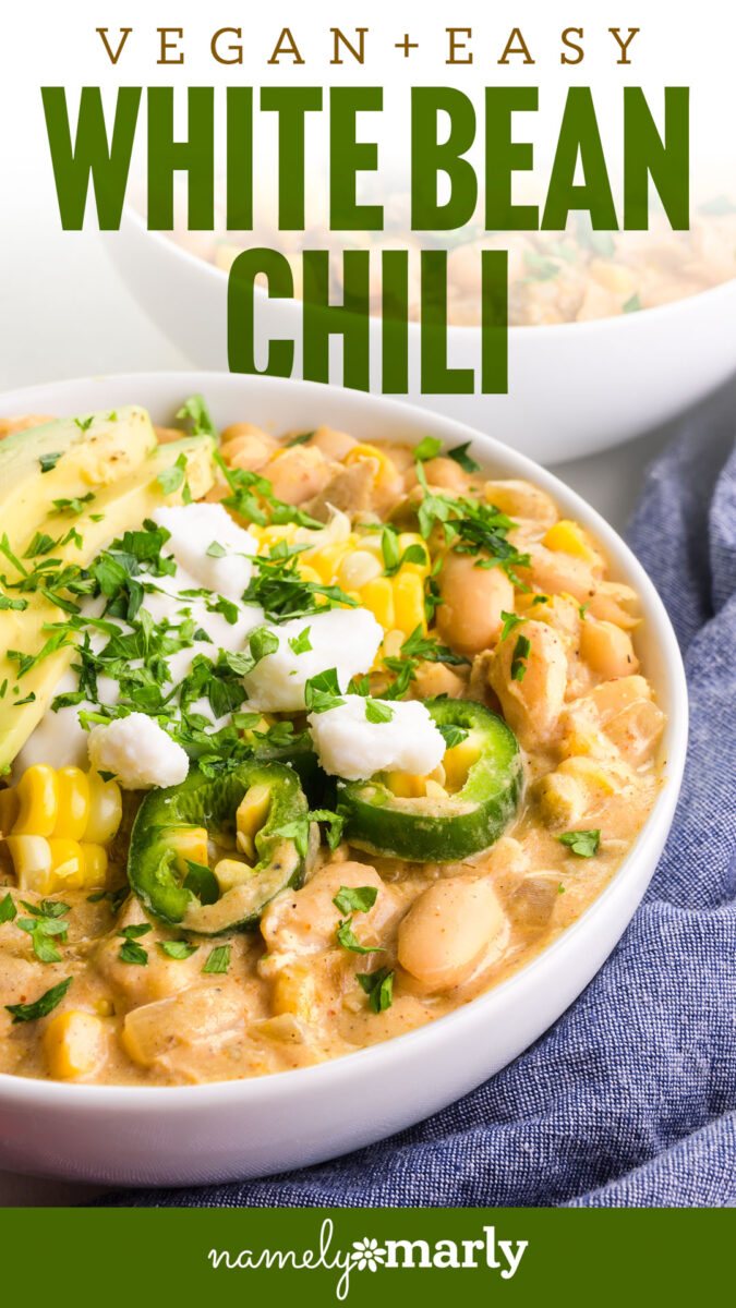 Vegan white bean chili topped with avocado, corn, jalapeño, cilantro, and dollops of cream in a white bowl.
