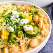 A bowl of white bean chili is topped with sour cream, sliced jalapeños, and other veggies.