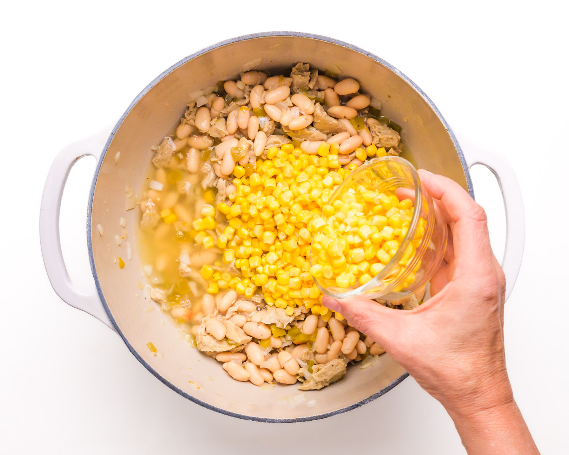 A hand pours corn into a pan with other ingredients.
