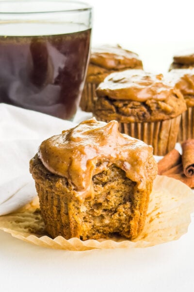a frosted pumpkin banana muffin with a bite taken out and several muffins behind it