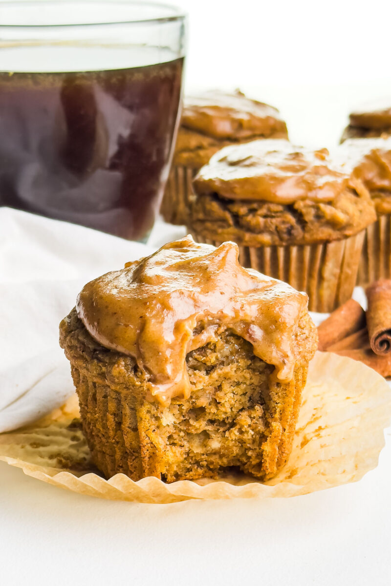 a frosted pumpkin banana muffin with a bite taken out and several muffins behind it