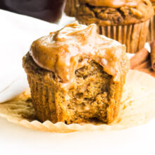 Frosted cupcake with a bite taken, showcasing a moist texture and cinnamon accents in the background.