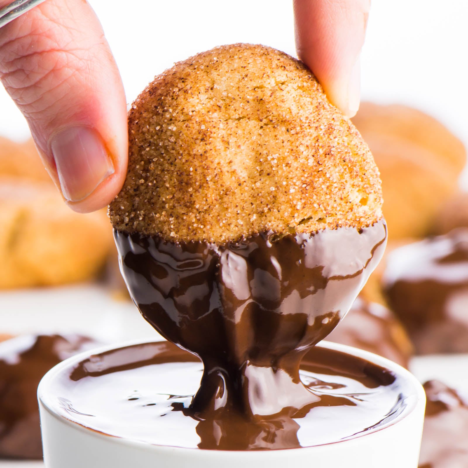 A snickerdoodle cookie is being dipped in melted dark chocolate.