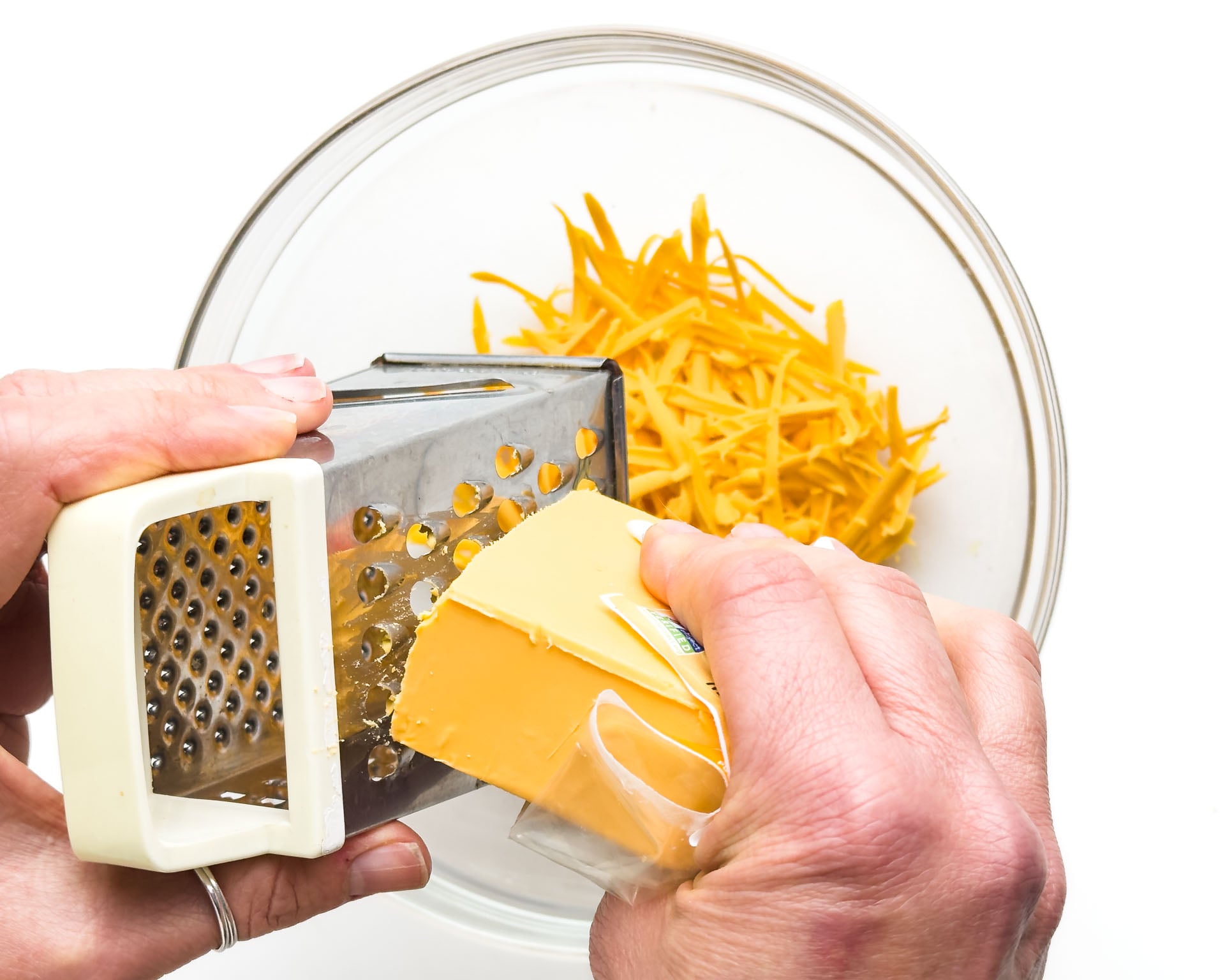 A hand holds a block of cheese grating it into a bowl.