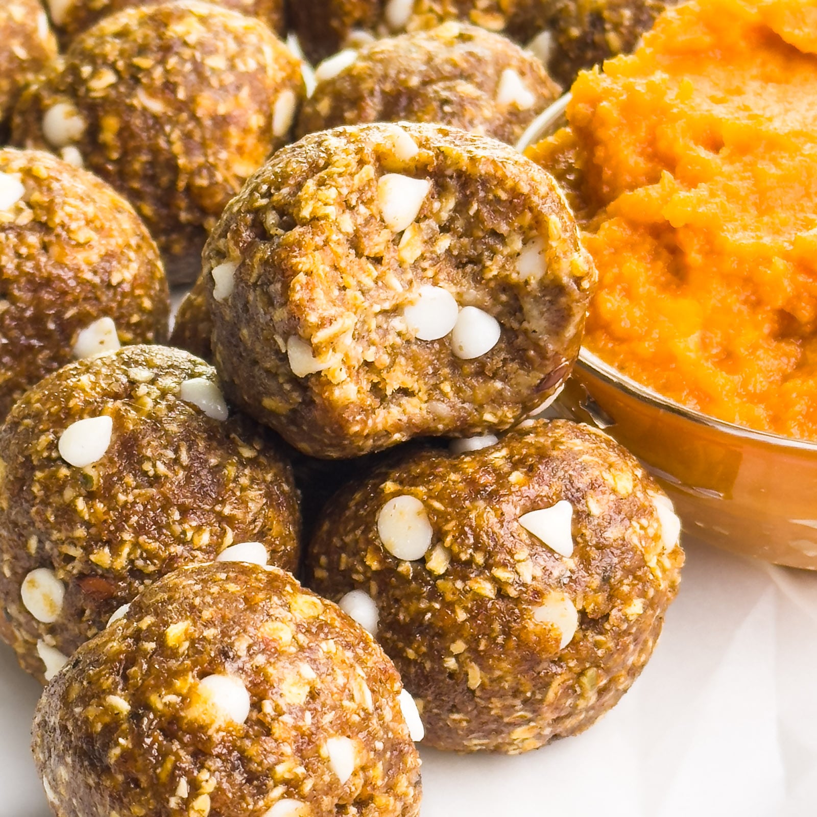 Pumpkin pie energy balls are next to a bowl of pumpkin puree, one with a bite taken out.