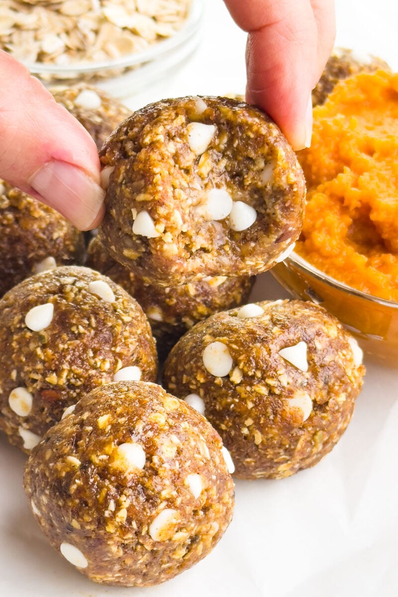 A hand holds a pumpkin pie energy ball with a bite taken out.