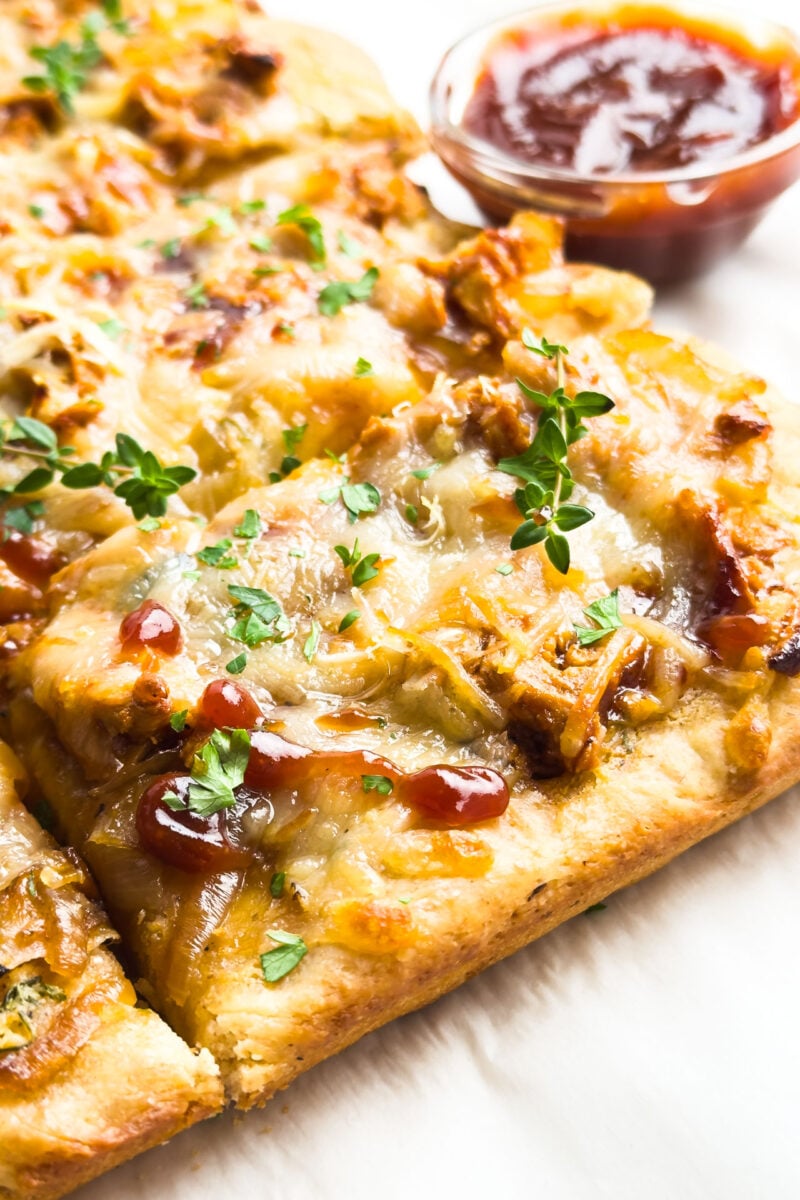 Slices of BBQ pizza sit in front of a bowl of BBQ sauce.
