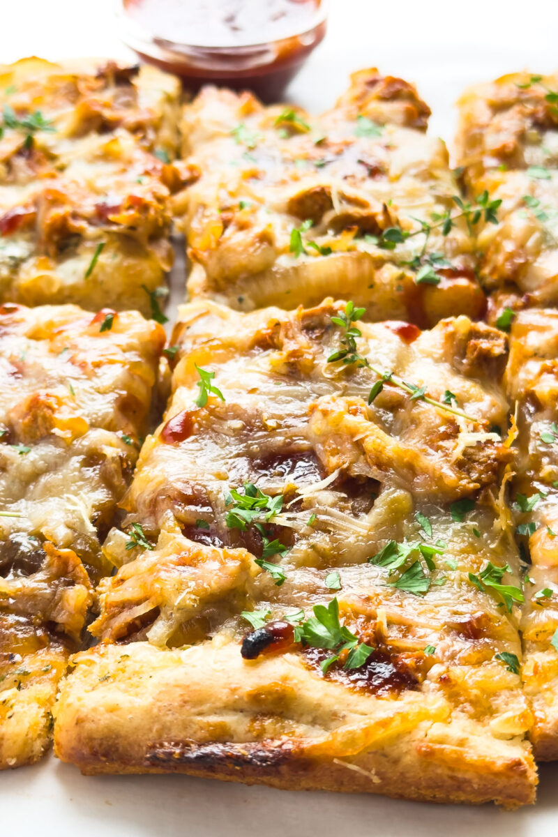 Slices of pizza sit in front of a bowl of BBQ sauce.