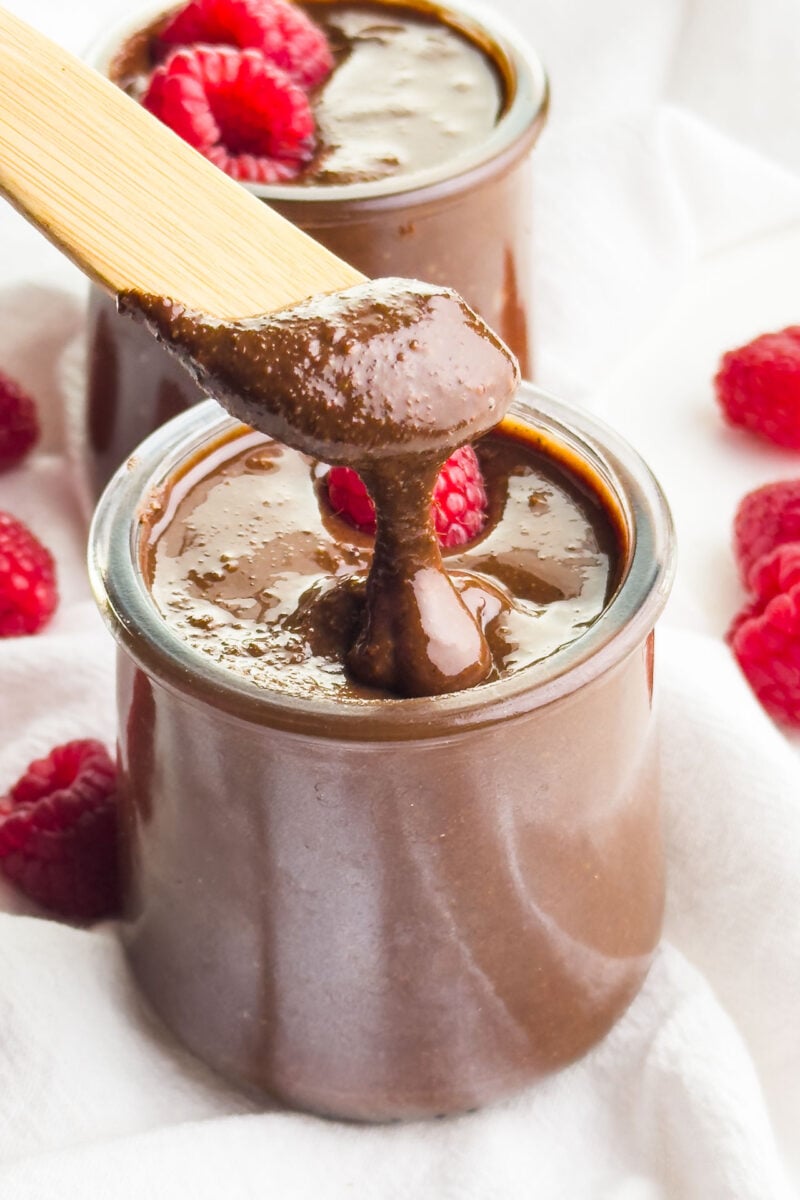 A serving utensil drizzles chocolate Nutella from a jar full of the nut butter spread.