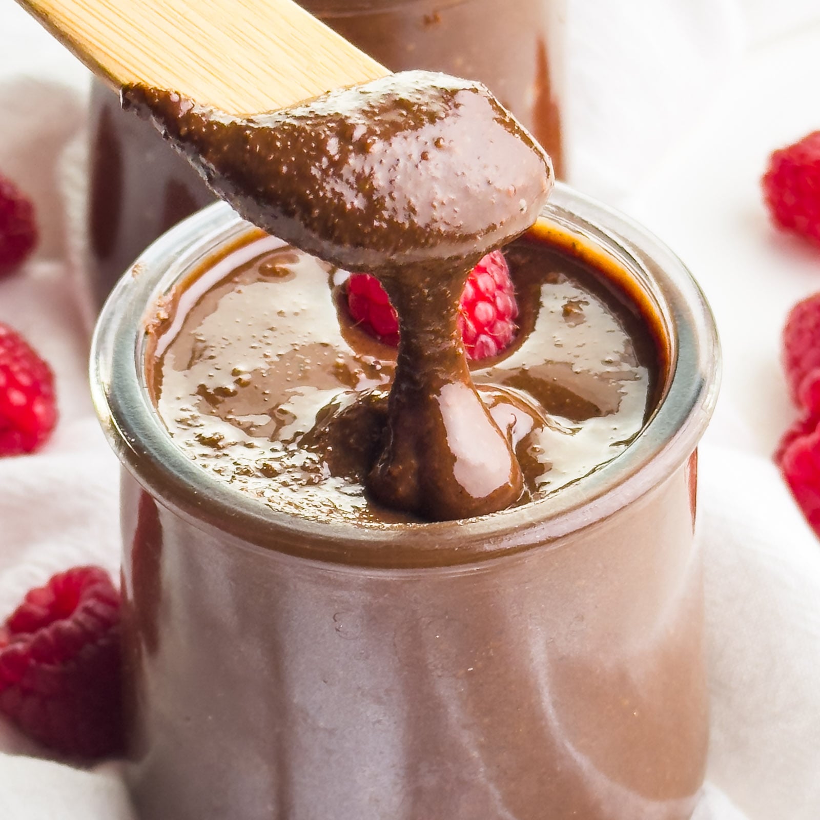 A closeup of chocolate hazelnut spread being dished out with a utensil from a jar.