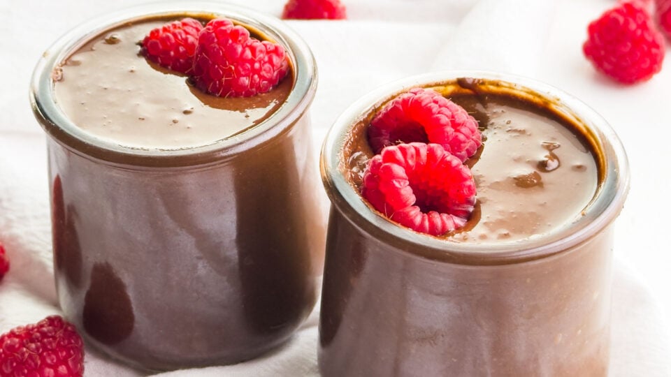Two jars of vegan chocolate Nutella spread have raspberries on top.