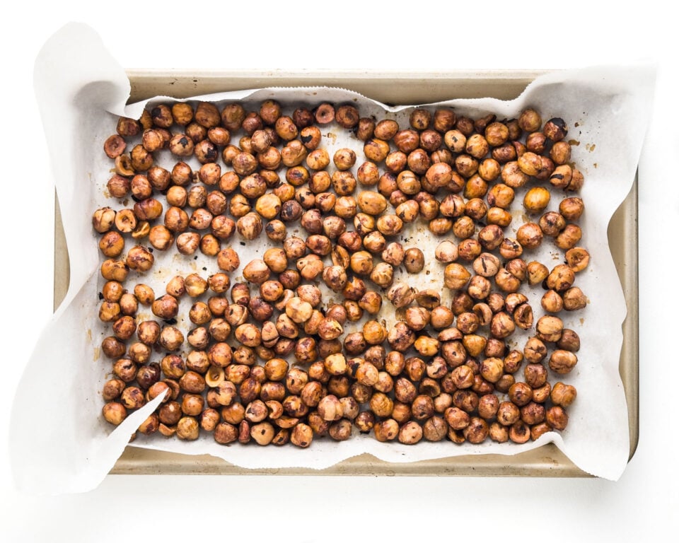 A baking pan is lined with parchment paper and covers with shelled hazelnuts.