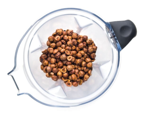Looking down on a blender jar filled with roasted, shelled hazelnuts.