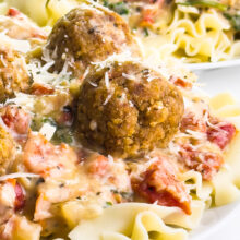 Noodles topped with creamy sauce, meatballs, and garnished with grated cheese and herbs.