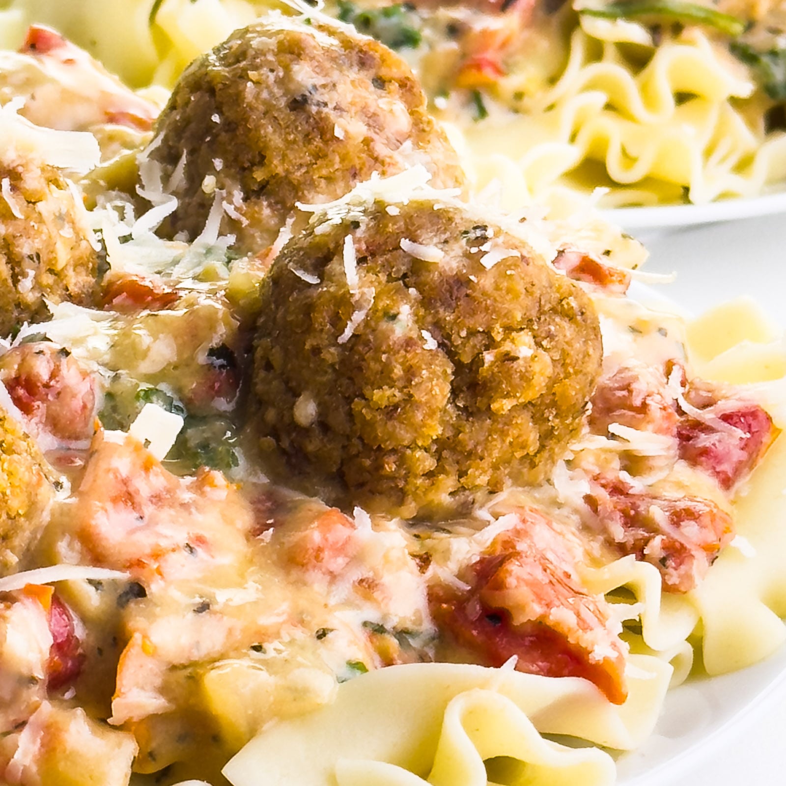 Noodles topped with creamy sauce, meatballs, and garnished with grated cheese and herbs.