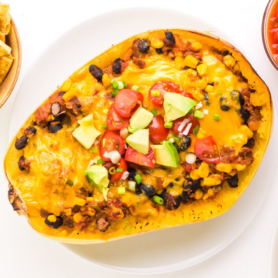 Looking down on a spaghetti squash with mexican filling and topped with cheese and other ingredients.