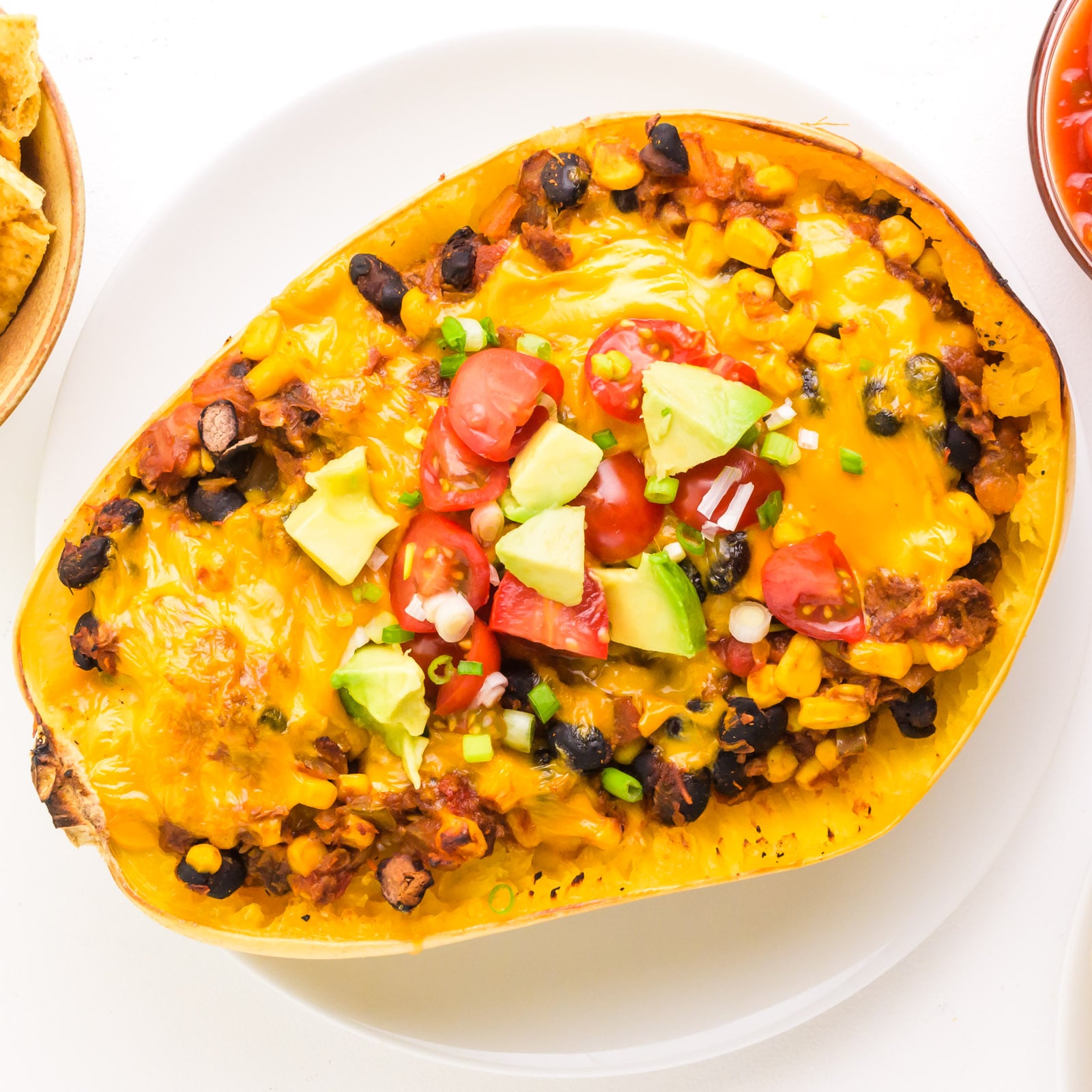 Looking down on a spaghetti squash with mexican filling and topped with cheese and other ingredients.