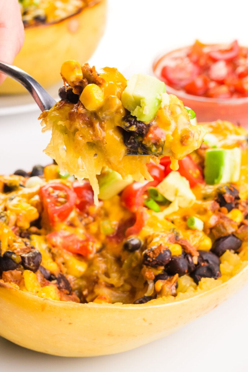 A forkful of spaghetti squash with mexican toppings, hovers over the rest of the plate of food.