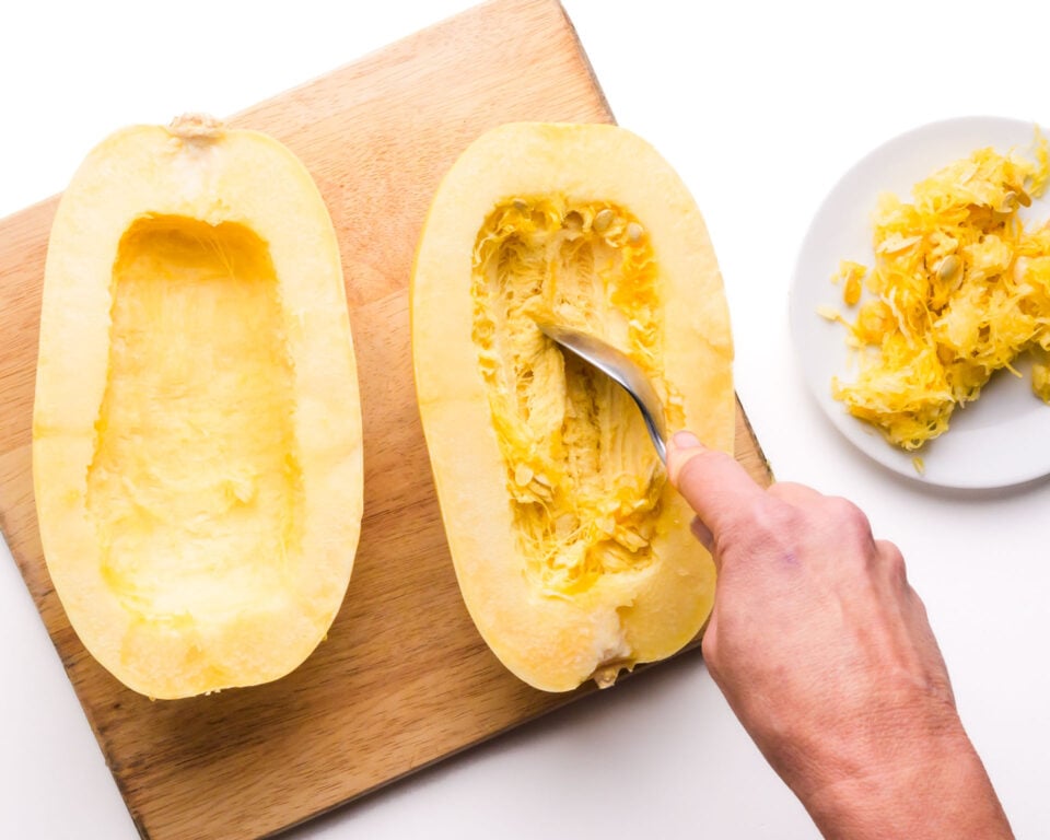 The insides of a spaghetti squash are being scraped of with a spoon.
