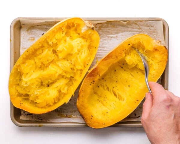 Roasted spaghetti squash on a pan is being fluffed with a fork.