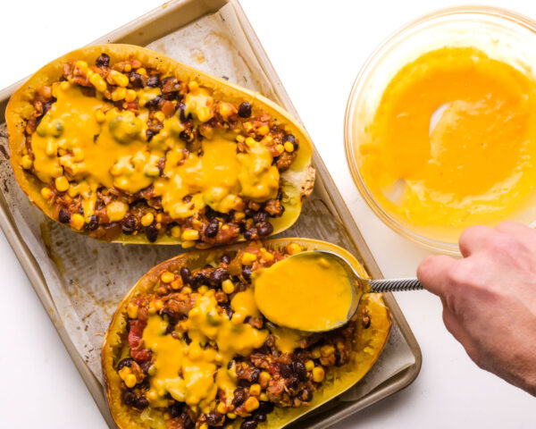 Melted cheese is drizzled over spaghetti squash bowls in a baking pan.