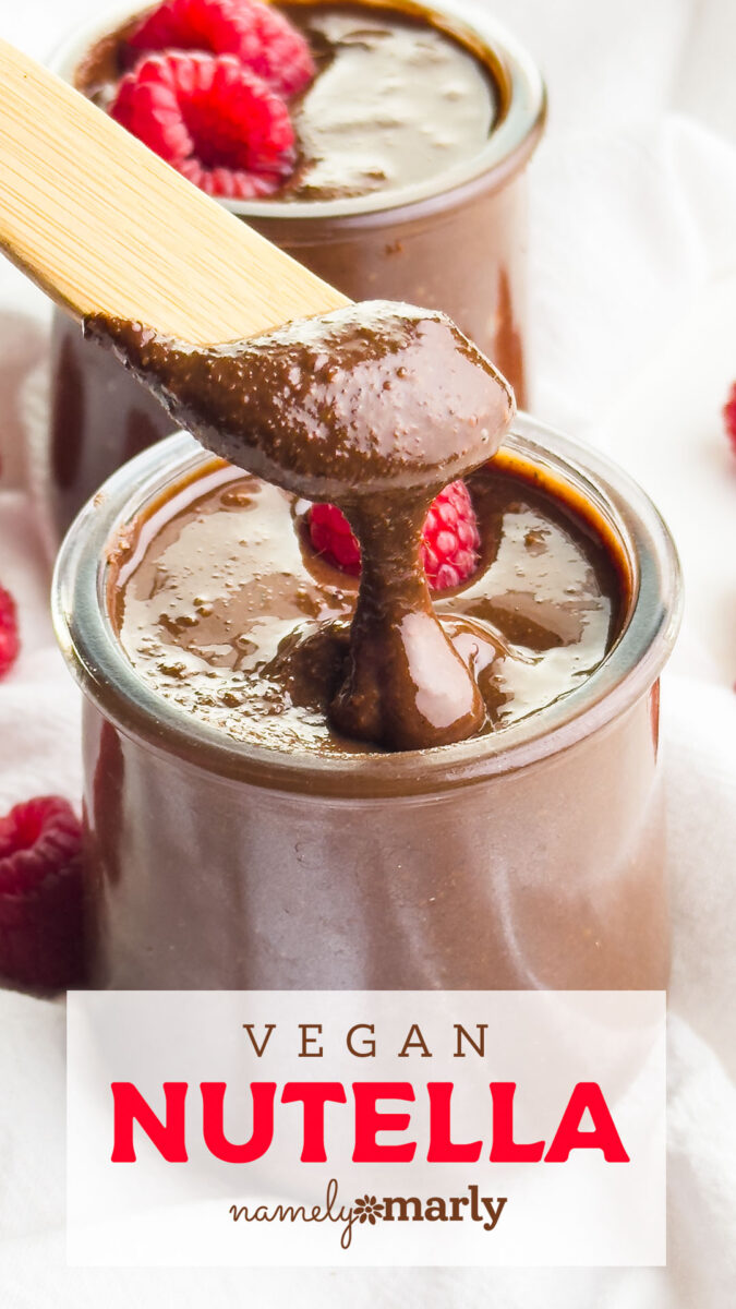 A wooden spoon drizzles vegan Nutella from a glass jar, garnished with raspberries on a light background.