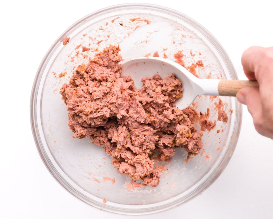 A hand stirs vegan sausage mixture in a bowl.