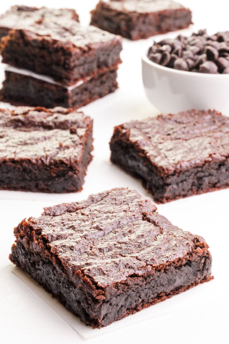 Several slices of chickpea brownies are surrounding a bowl of chocolate chips.