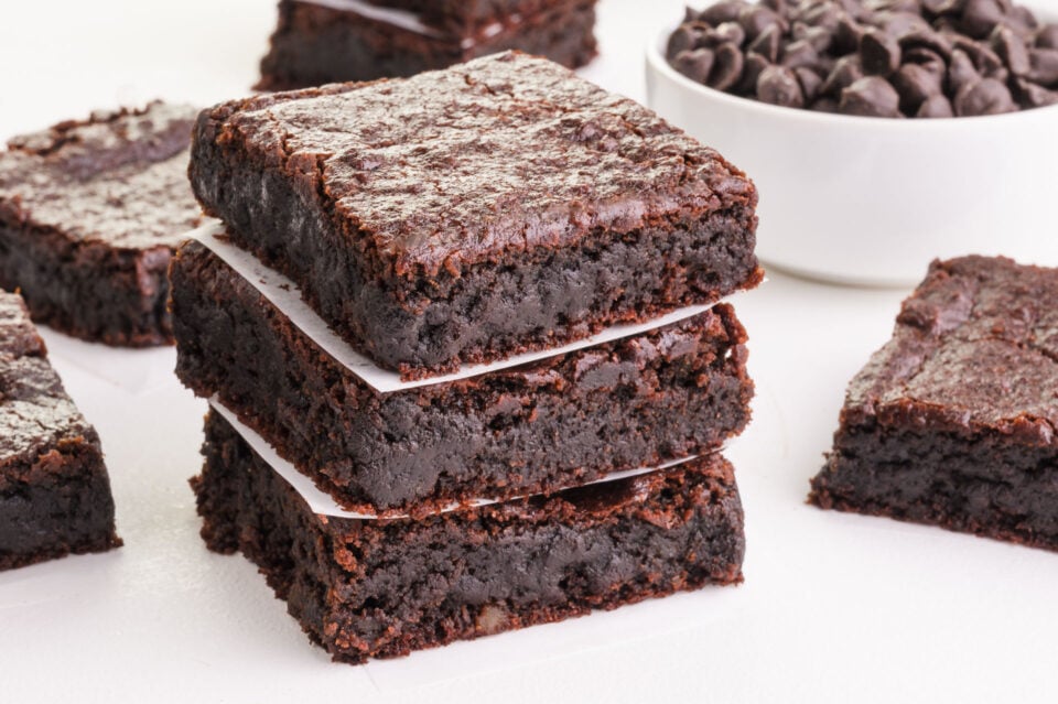 A stack of chickpea brownies sits near other slices and a bowl of chocolate chips.