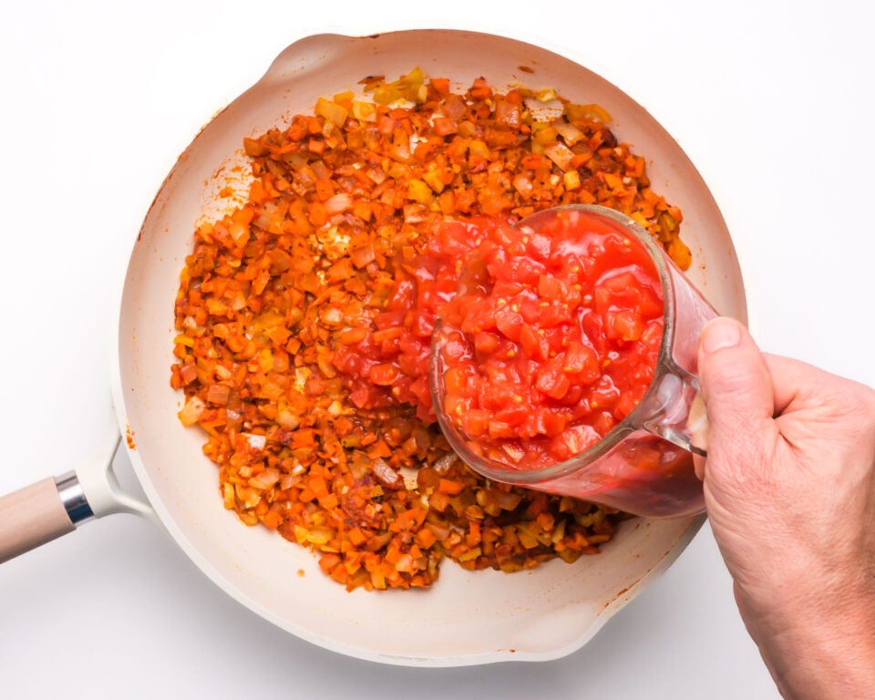 Diced tomatoes are being poured into a pan with a red sauce.