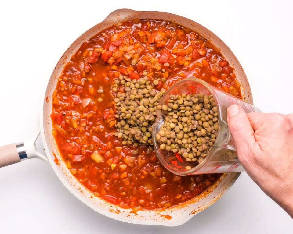 Lentils are being poured into a pan with red sauce.