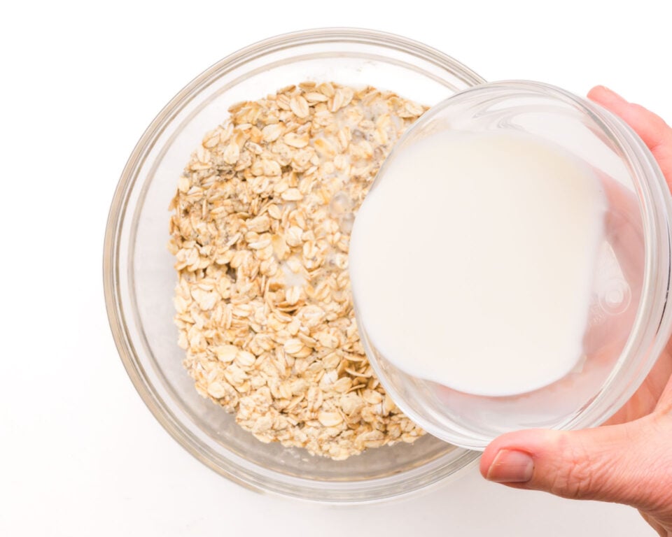 Milk is being poured from a smaller bowl into a bowl with oats.