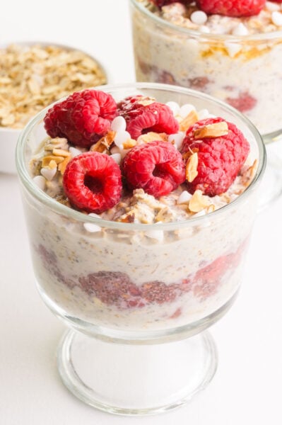 A bowl of raspberry overnight oats sits in front of oats and another bowl of the overnight oats.