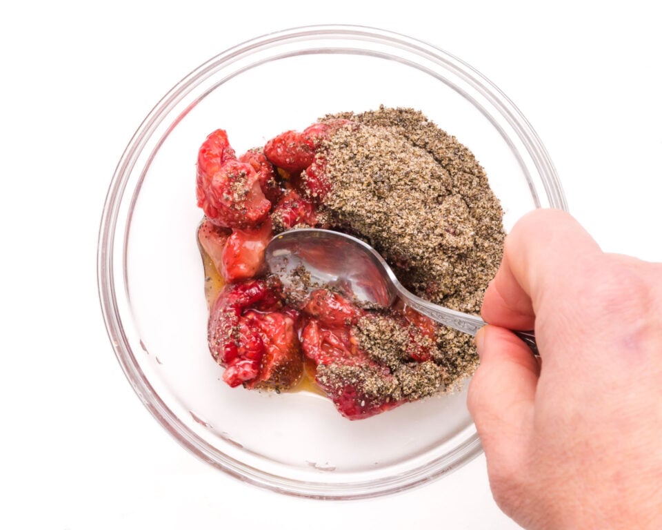 A hand stirs chia seeds and raspberries together.