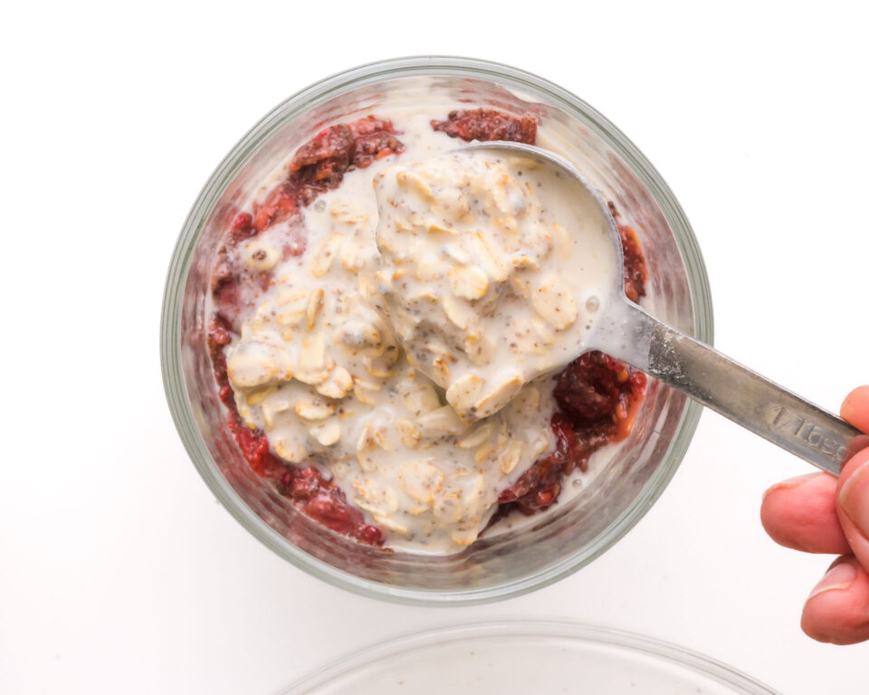 A layer of overnight oats is being added over a raspberry layer.