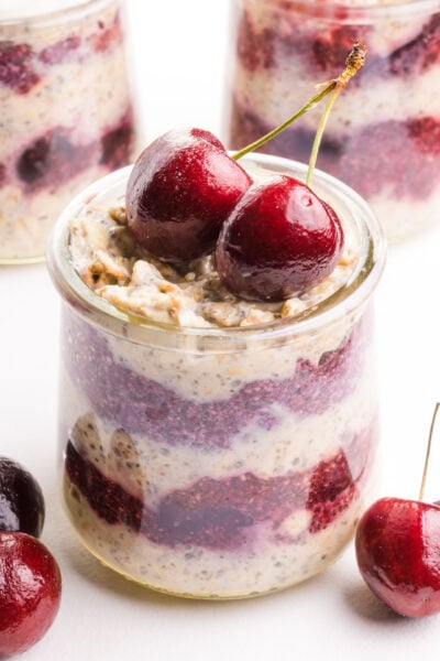 A closeup of layered cherry overnight oats in a jar with fresh cherries on top.